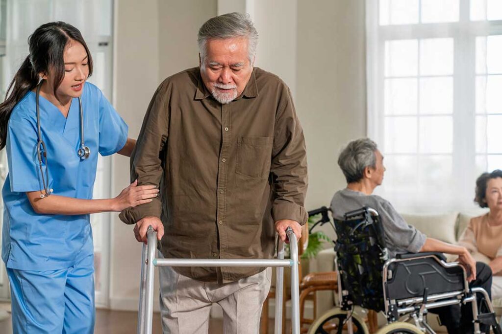 Two older adults sitting together in a bright common room, talking calmly with a staff member nearby.